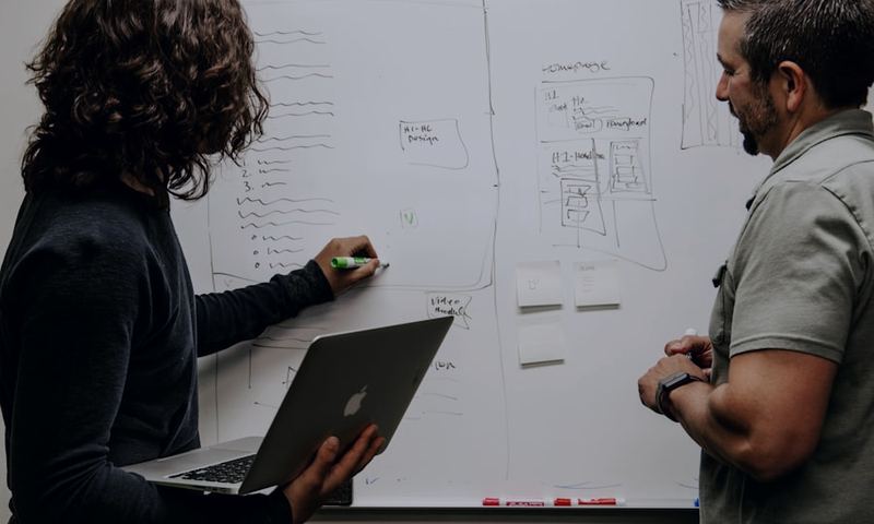 A facilitator mapping ideas on a whiteboard while a colleague looks on