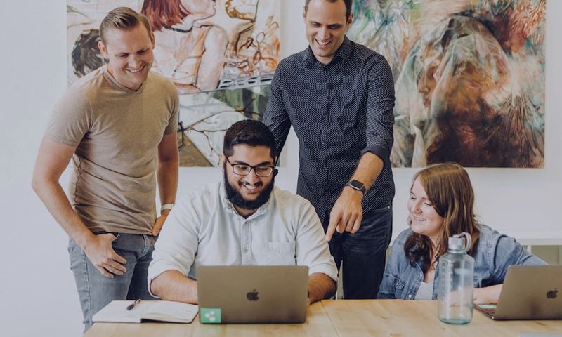 Four coworkers laughing together around a laptop