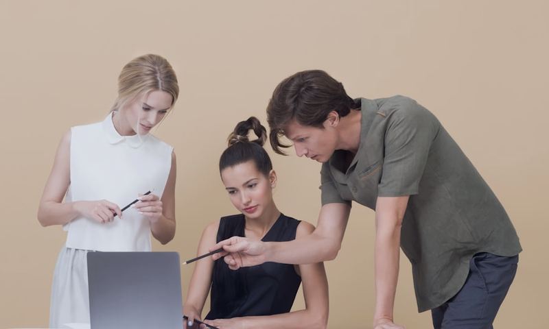 A colleague explaining something on a laptop to a teammate